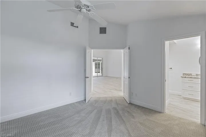 Unfurnished bedroom featuring light carpet, vaulted ceiling, and ceiling fan