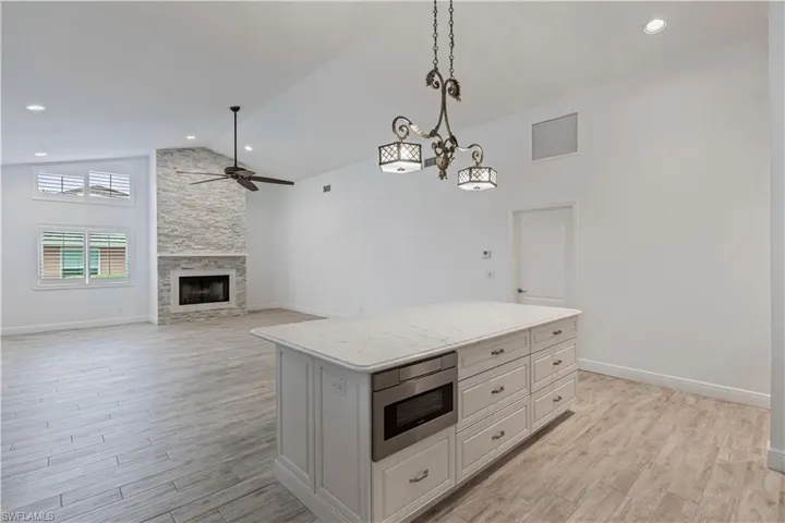 Kitchen featuring ceiling fan with notable chandelier, decorative light fixtures, light hardwood / wood-style flooring, a stone fireplace, and white cabinetry