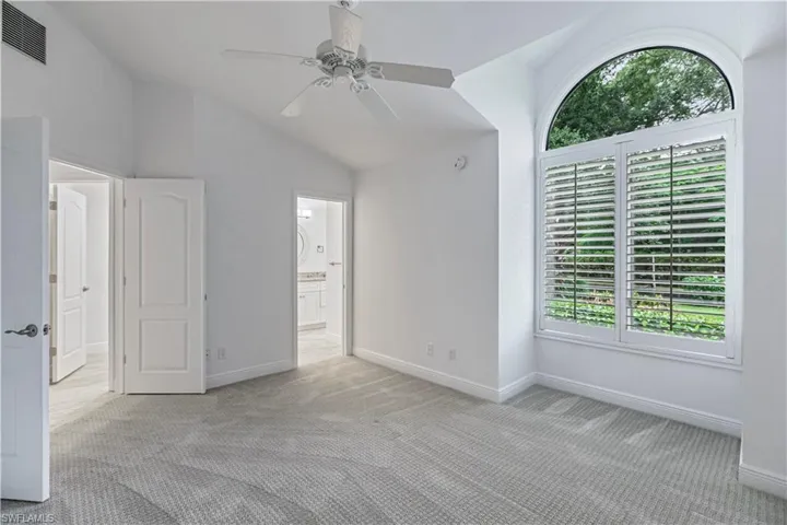 Unfurnished bedroom with light colored carpet, vaulted ceiling, ceiling fan, and connected bathroom