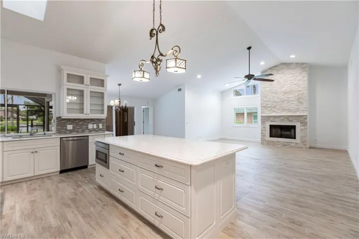 Kitchen with decorative light fixtures, ceiling fan with notable chandelier, stainless steel appliances, a stone fireplace, and tasteful backsplash