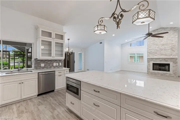 Kitchen with ceiling fan with notable chandelier, a fireplace, stainless steel appliances, white cabinetry, and lofted ceiling
