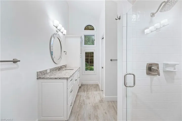 Bathroom featuring vanity, lofted ceiling, wood-type flooring, and a shower with door