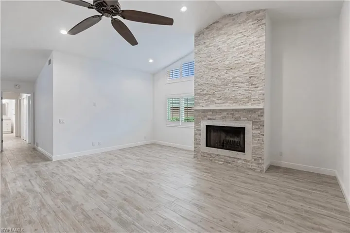 Unfurnished living room with high vaulted ceiling, ceiling fan, a stone fireplace, and light wood-type flooring