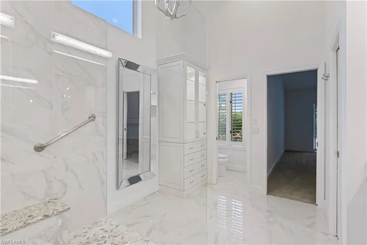 Bathroom with tiled shower, toilet, and a towering ceiling