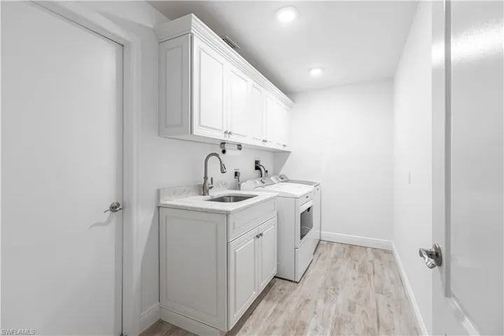 Laundry area with light wood-type flooring, cabinets, independent washer and dryer, and sink