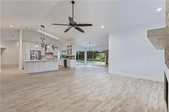 Unfurnished living room with high vaulted ceiling, ceiling fan with notable chandelier, and light hardwood / wood-style floors