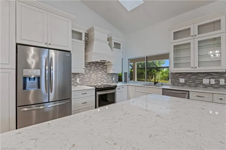 Kitchen featuring stainless steel appliances, light stone countertops, custom exhaust hood, and lofted ceiling with skylight