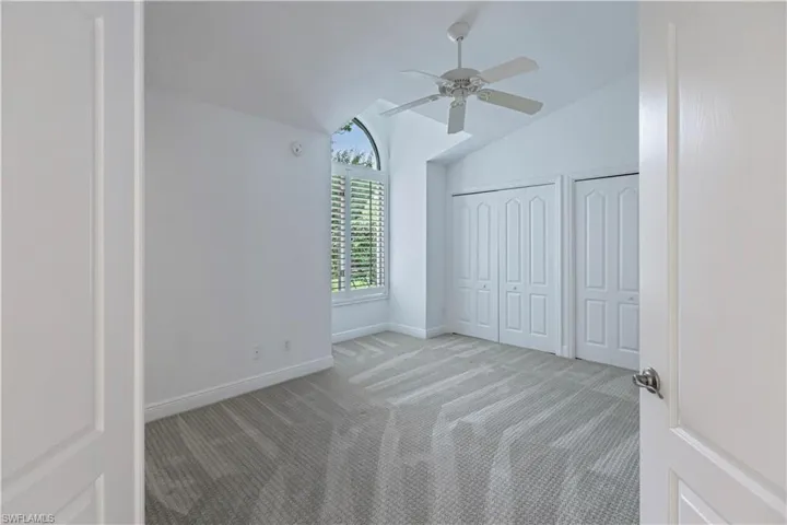 Unfurnished bedroom featuring multiple closets, ceiling fan, light carpet, and vaulted ceiling
