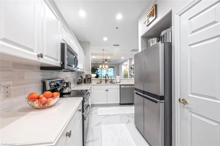 Kitchen featuring appliances with stainless steel finishes, a peninsula, marble finish floor, white cabinetry, and a sink