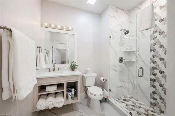Full bathroom featuring toilet, a skylight, vanity, marble finish floor, and a marble finish shower