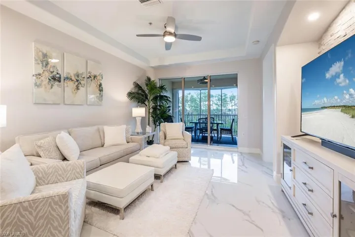 Living room with a ceiling fan, marble finish floor, a raised ceiling, and baseboards