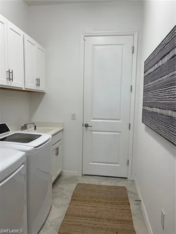 Laundry room featuring cabinets, sink, light tile flooring, and washing machine and clothes dryer