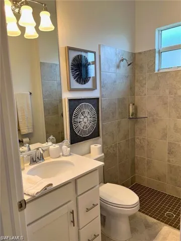 Bathroom featuring tiled shower, toilet, tile floors, and large vanity