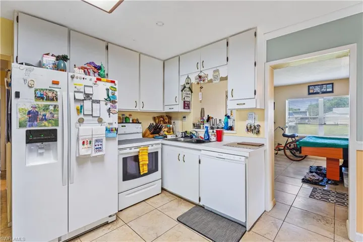 Kitchen featuring white cabinetry, light countertops, a sink, white appliances, and light tile patterned flooring