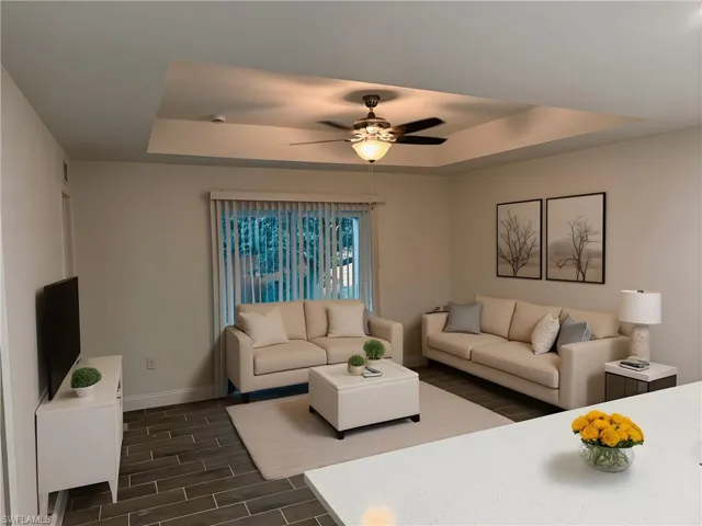 Living area featuring a raised ceiling, wood finish floors, and a ceiling fan