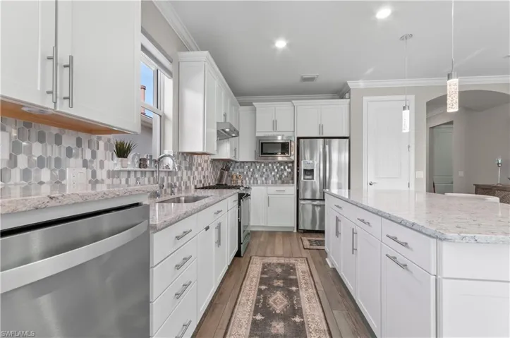 Kitchen with a center island, pendant lighting, decorative backsplash, white cabinets, and appliances with stainless steel finishes