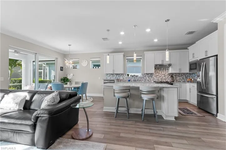 Kitchen featuring hanging light fixtures, appliances with stainless steel finishes, a kitchen island, a kitchen bar, and white cabinetry