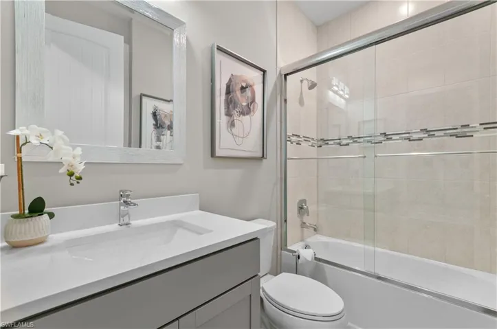 Full bathroom featuring shower / bath combination with glass door, vanity, and toilet