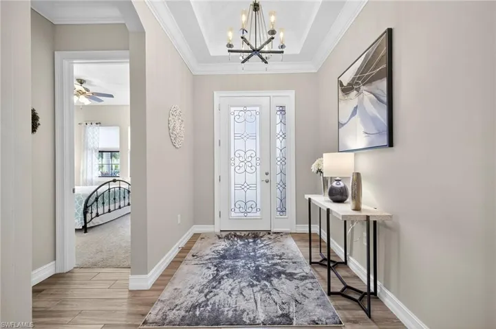 Entryway with light wood-type flooring, a chandelier, ornamental molding, a raised ceiling, and ceiling fan