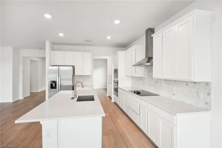 Kitchen with stainless steel appliances, light wood-type flooring, wall chimney range hood, sink, and an island with sink