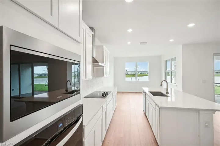 Kitchen featuring sink, black appliances, a kitchen island with sink, white cabinets, and light wood-type flooring