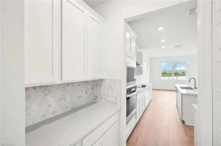 Kitchen featuring white cabinets, light hardwood / wood-style flooring, sink, light stone countertops, and appliances with stainless steel finishes