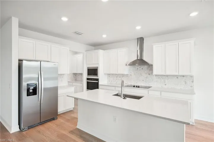 Kitchen with white cabinets, light wood-type flooring, appliances with stainless steel finishes, and wall chimney range hood
