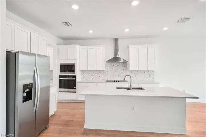 Kitchen with an island with sink, white cabinets, wall chimney exhaust hood, and stainless steel appliances