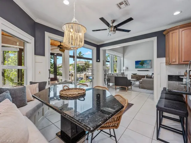 Dining area with a ceiling fan, light tile patterned flooring, a chandelier, a wainscoted wall, and crown molding