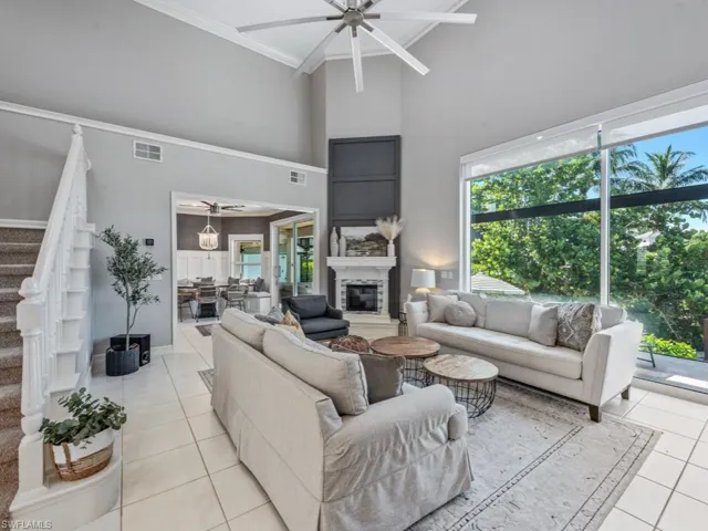 Living room featuring ceiling fan, a high ceiling, light tile patterned flooring, stairs, and a glass covered fireplace