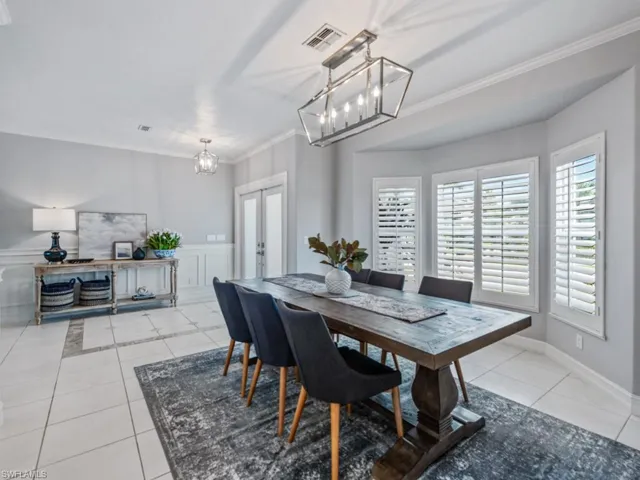 Dining room featuring a chandelier, light tile patterned floors, crown molding, french doors, and wainscoting