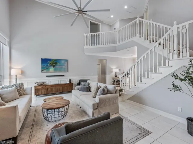 Living room with a towering ceiling, a ceiling fan, stairs, crown molding, and wainscoting