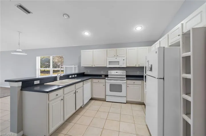 Kitchen with white appliances, dark countertops, white cabinets, pendant lighting, and light tile patterned flooring