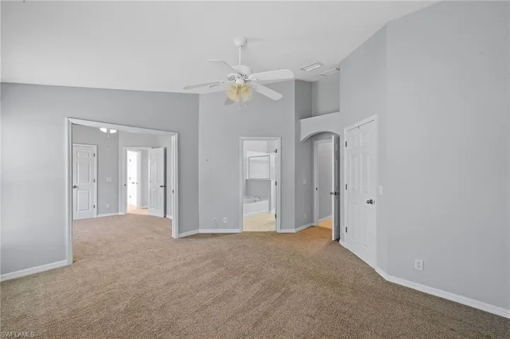 Unfurnished bedroom featuring light carpet, ensuite bath, high vaulted ceiling, and ceiling fan
