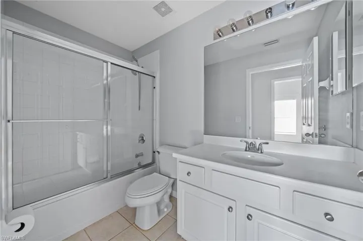 Full bath with vanity, shower / bath combination with glass door, and light tile patterned floors