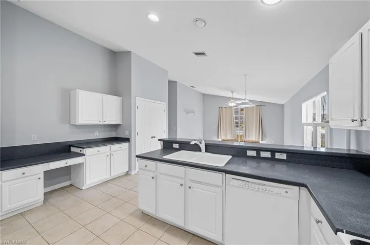Kitchen with dishwasher, white cabinetry, dark countertops, light tile patterned floors, and lofted ceiling