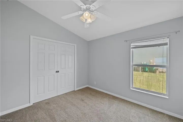 Unfurnished bedroom featuring lofted ceiling, a closet, light colored carpet, and ceiling fan