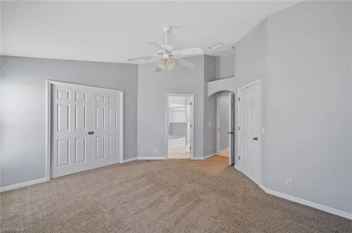Unfurnished bedroom with a closet, high vaulted ceiling, light colored carpet, ensuite bath, and a ceiling fan