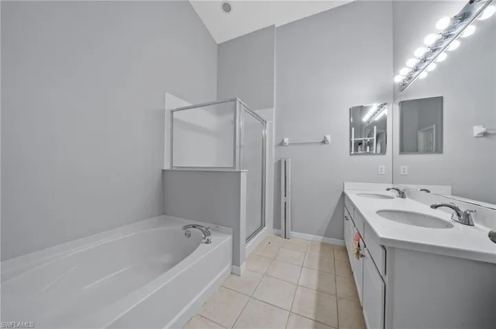 Bathroom featuring a bath, double vanity, light tile patterned floors, a shower stall, and vaulted ceiling