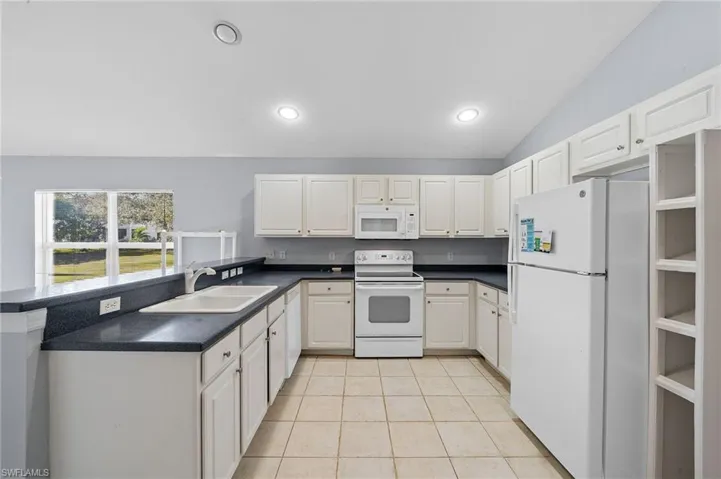 Kitchen with white appliances, dark countertops, white cabinets, light tile patterned floors, and lofted ceiling