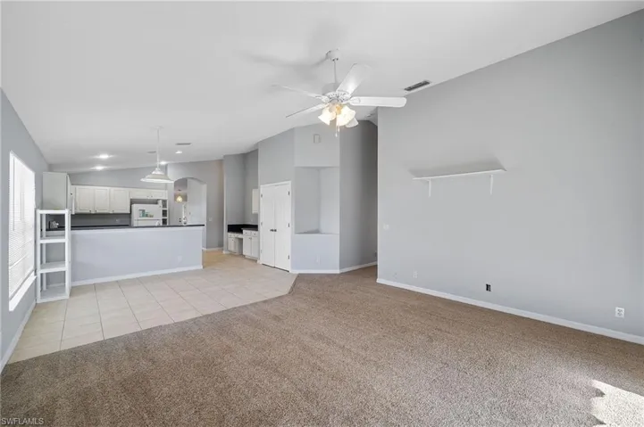 Unfurnished living room with vaulted ceiling, arched walkways, light colored carpet, light tile patterned floors, and ceiling fan