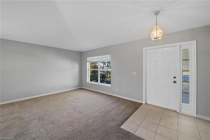 Foyer with light colored carpet, light tile patterned flooring, and lofted ceiling
