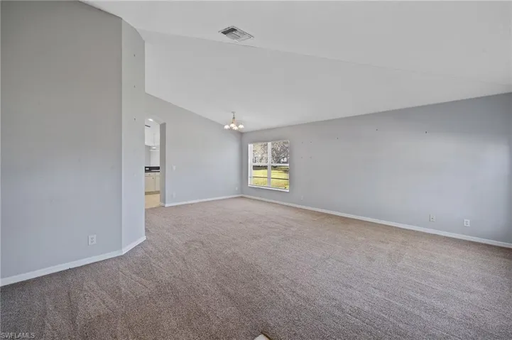 Unfurnished room with lofted ceiling, a chandelier, and light colored carpet