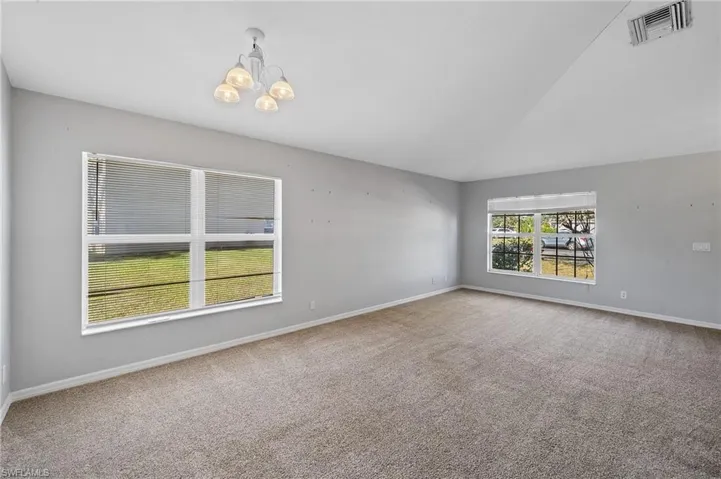 Carpeted spare room with lofted ceiling and a chandelier