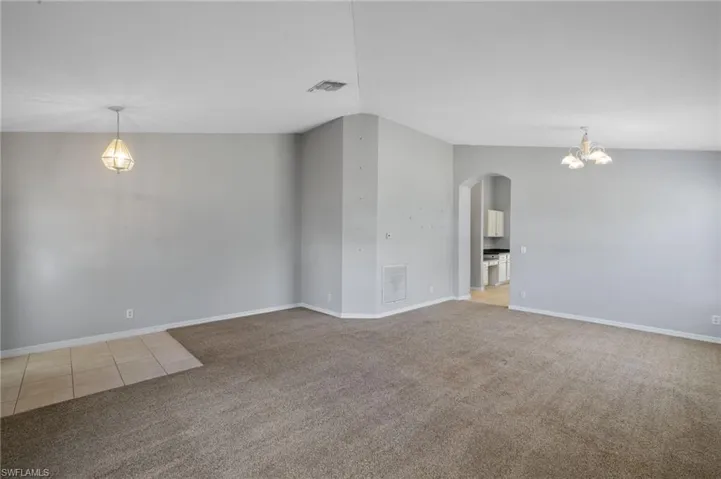 Unfurnished room featuring arched walkways, a chandelier, and light carpet