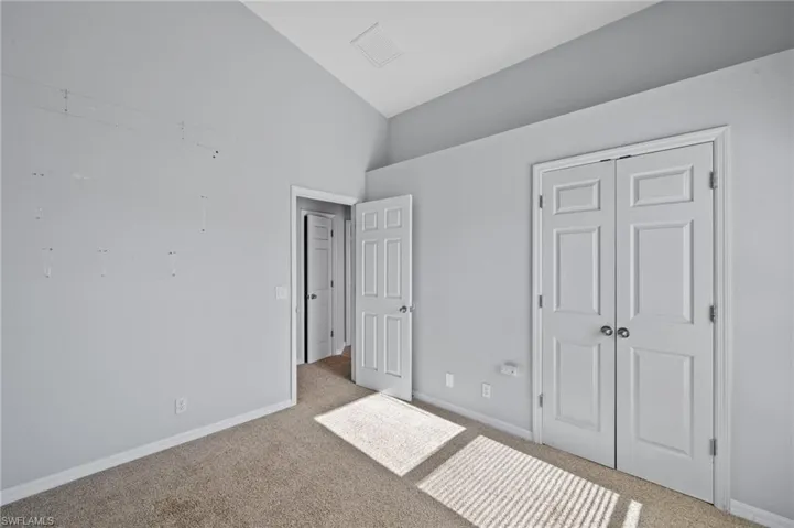 Unfurnished bedroom featuring carpet flooring, a closet, and high vaulted ceiling