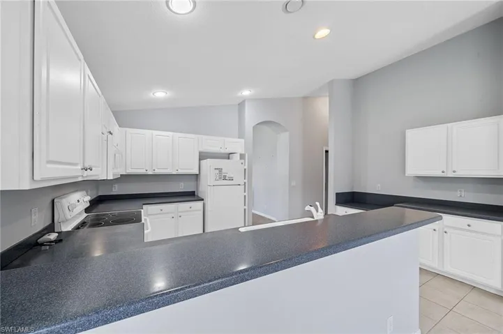 Kitchen with dark countertops, white cabinets, white appliances, vaulted ceiling, and recessed lighting
