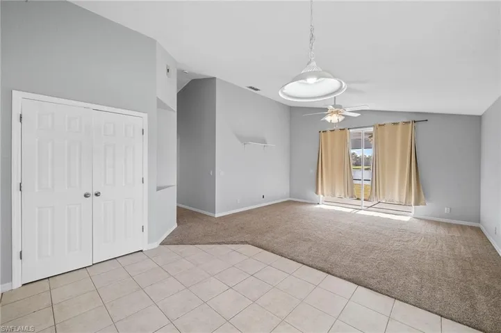 Unfurnished living room with light carpet, lofted ceiling, ceiling fan, and light tile patterned floors