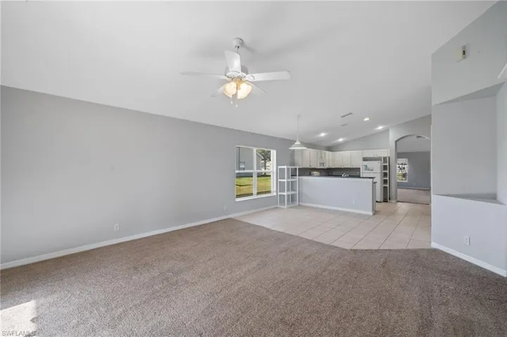 Unfurnished living room featuring lofted ceiling, light carpet, arched walkways, light tile patterned flooring, and ceiling fan