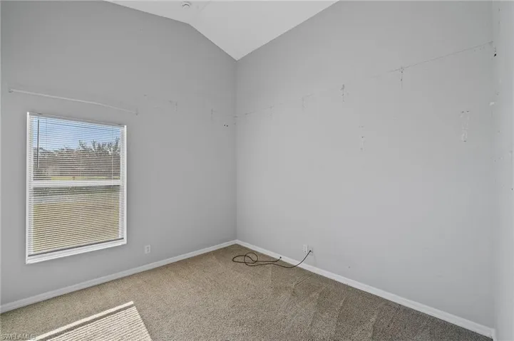Carpeted empty room featuring baseboards and vaulted ceiling